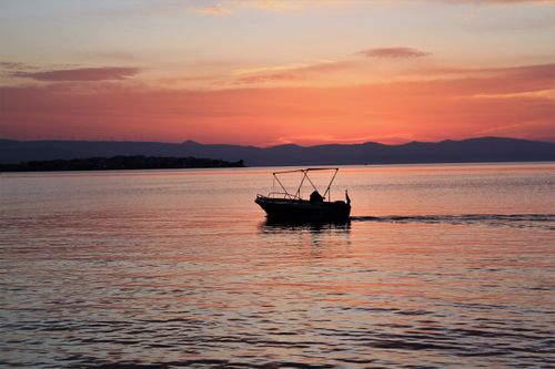 Free A serene sunset scene with a boat silhouetted against vibrant colors on calm water. Stock Photo