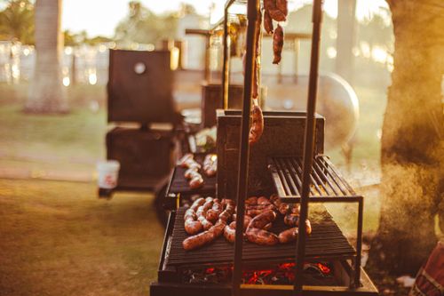 Free A warm, golden hour barbecue with various sausages grilling on an open fire outdoors. Stock Photo