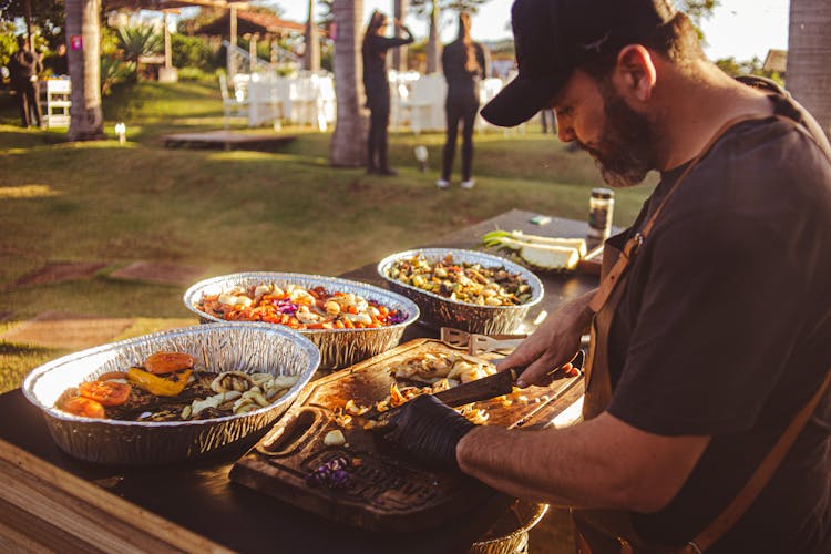 A Man Slicing Food On A Wooden Chopping Board