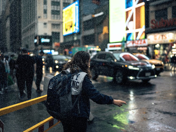 Grainy Photo Of Woman Wearing Backpack Walking Through Busy Street At Night