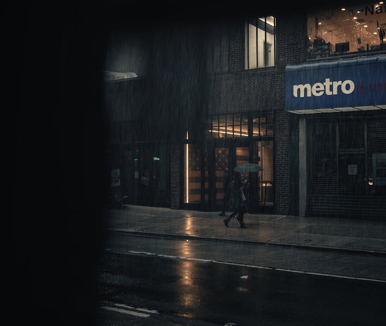 A Person Walking On A Sidewalk While Raining 