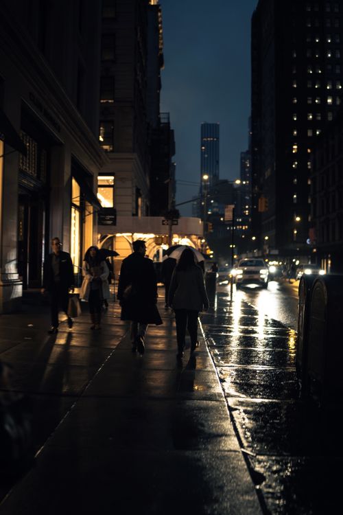 Free A nighttime city street with people walking on the sidewalk, lit by streetlights. Stock Photo