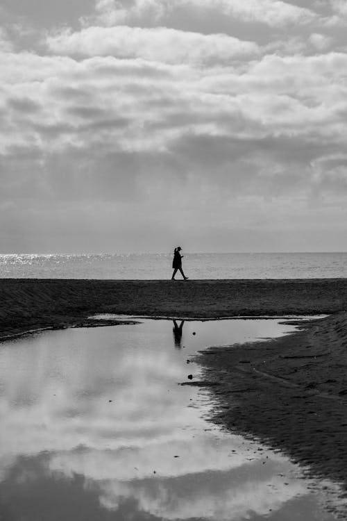 Grayscale Photo of a Woman Walking by the Sea