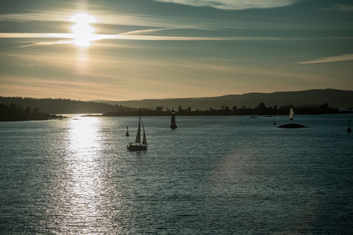Sailboats gliding on Oslo Fjord at sunset with a lighthouse in the distance
