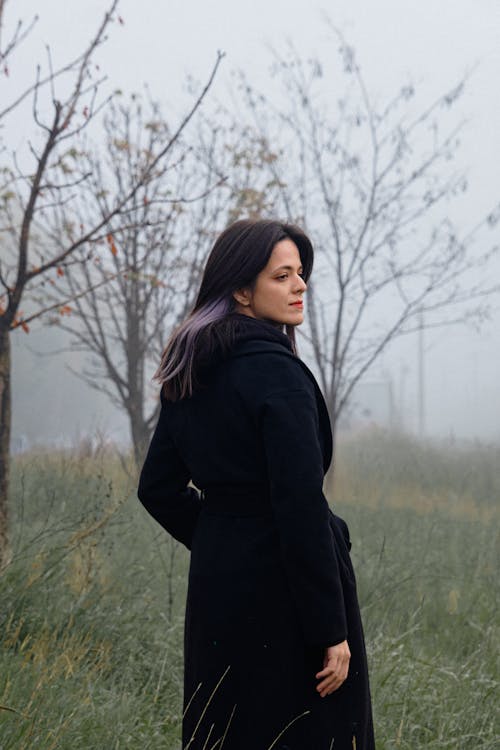 A Woman in Black Coat Standing on Green Grass Field