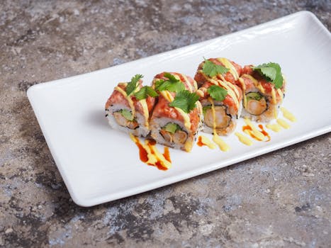 Close-up of sushi rolls garnished with sauce and cilantro on a white plate.