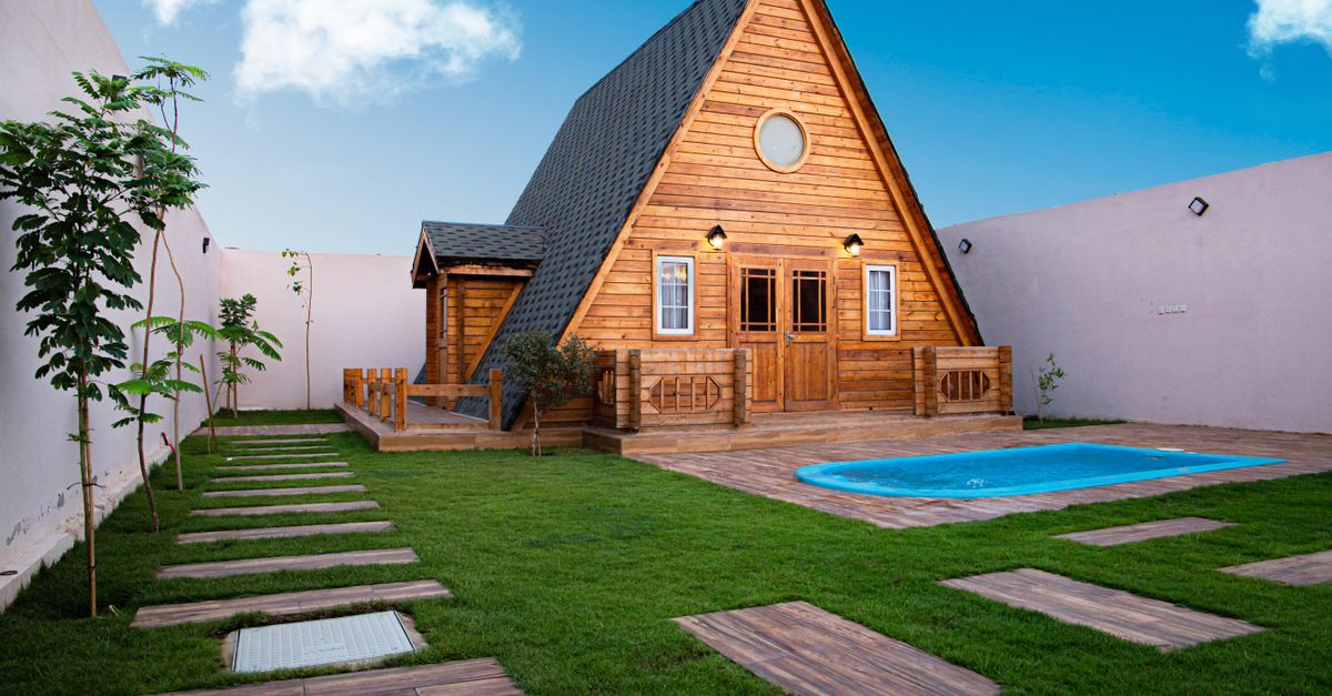A serene A-frame wooden cottage with a small pool and lush lawn, perfect for relaxation.