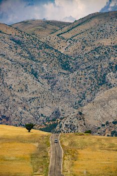 A car drives through a picturesque mountain landscape with open fields and trees.
