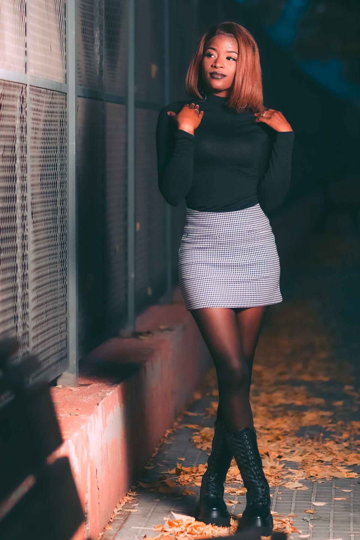 Confident woman posing by a metal fence in fashionable autumn attire. Modern fashion vibe.