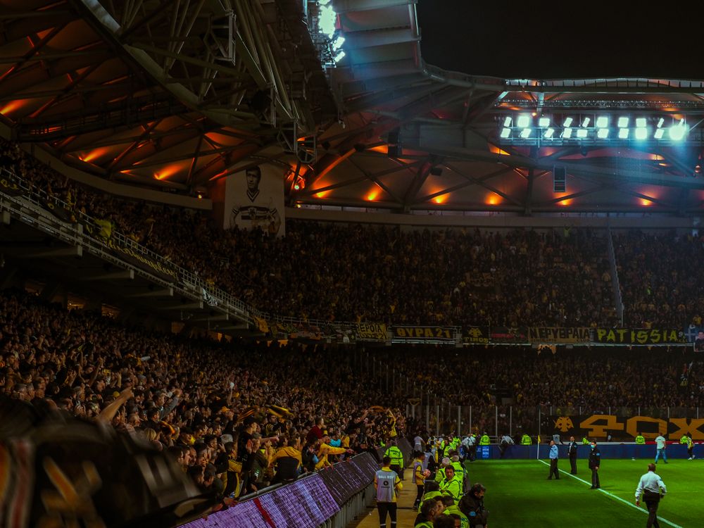 Excited football fans cheering in a stadium with colorful flags and scarves