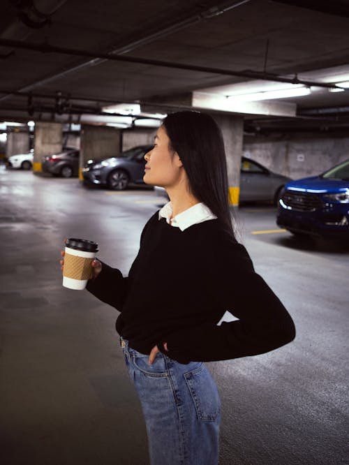 Woman in Black Long Sleeve Shirt and Blue Denim Jeans Holding White Disposable Cup