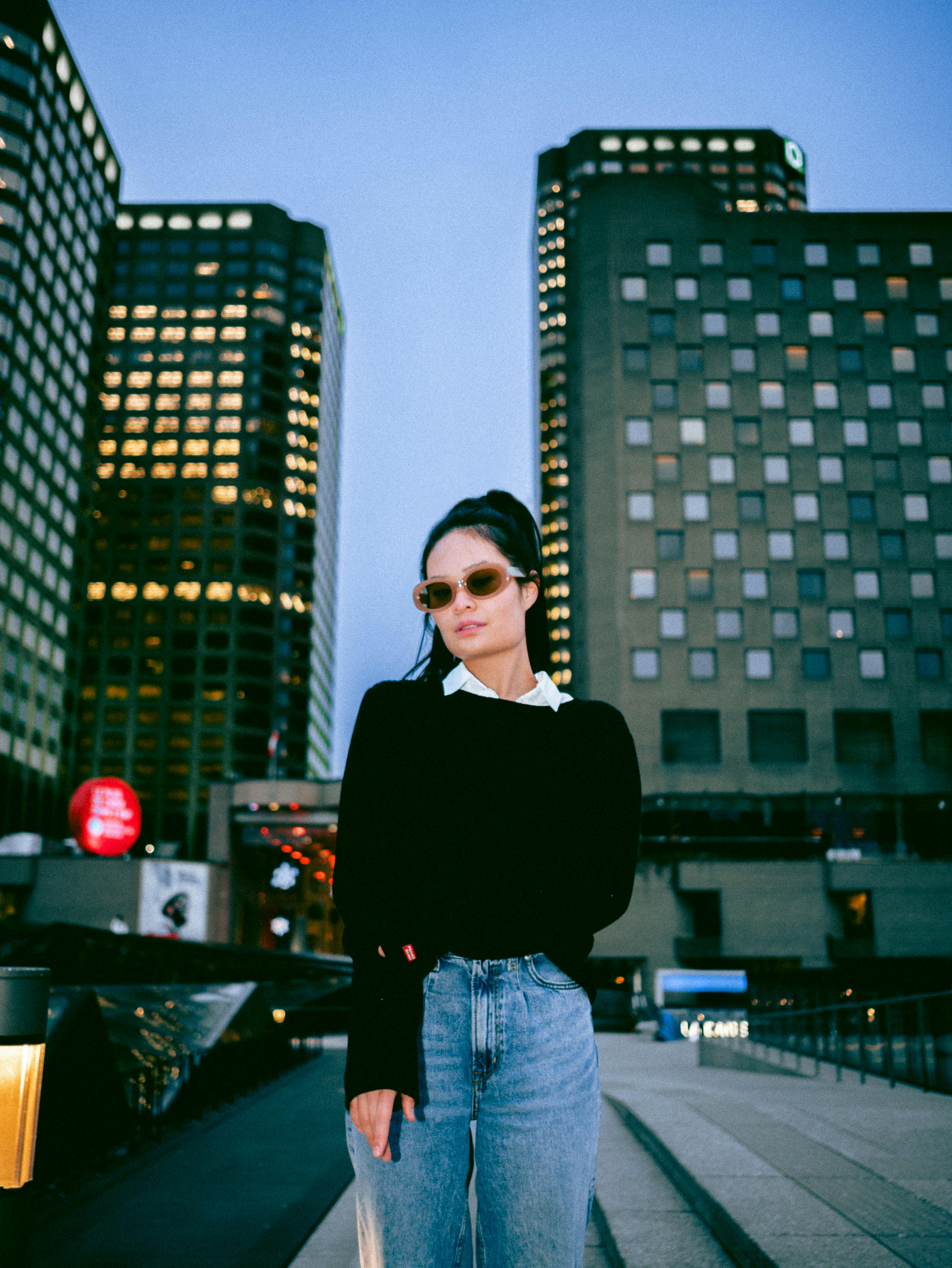 Fashionable woman in sunglasses against Montreal cityscape in the evening.