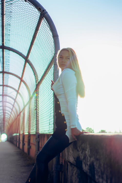 Woman in White Long Sleeve Shirt Sitting on a Concrete Barrier