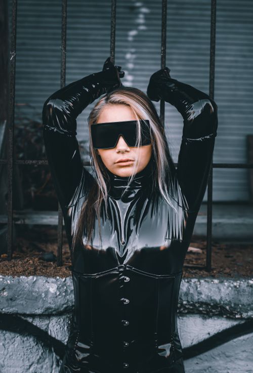Free Woman wearing a sleek black latex costume with sunglasses, embodying a futuristic style. Stock Photo