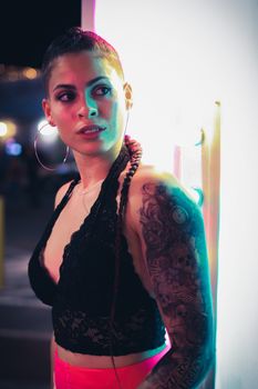 Portrait of a tattooed woman with hoop earrings in vibrant neon light.
