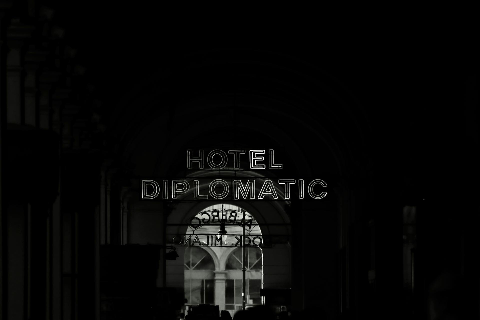 Black and white photo of the Hotel Diplomatic entrance at night, showcasing its glowing sign.