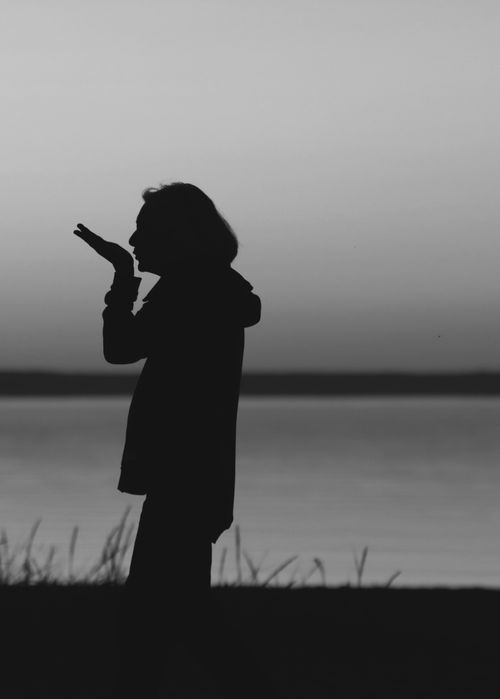 Free A striking silhouette of a person standing by a calm body of water during twilight. Stock Photo