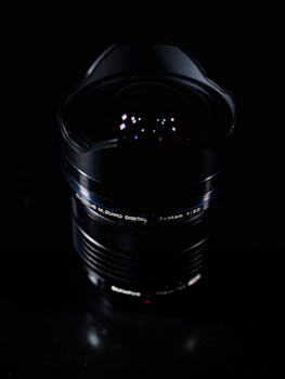 Moody close-up shot of a modern camera lens reflecting light against a dark setting.