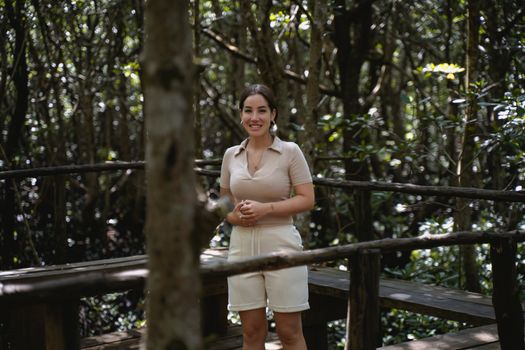 Smiling woman standing on a wooden boardwalk surrounded by thick foliage.