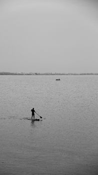 A lone silhouette paddleboarding on a tranquil water surface during a calm sunset.