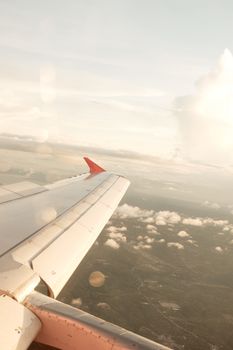A beautiful vertical shot of an airplane wing soaring above fluffy clouds with a scenic horizon.