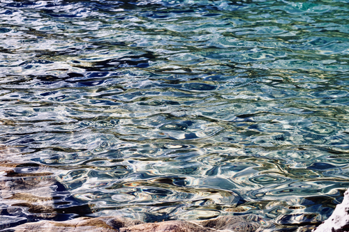 Free Close-up view of rippling water surface with clear reflections, bordering a rocky edge. Stock Photo
