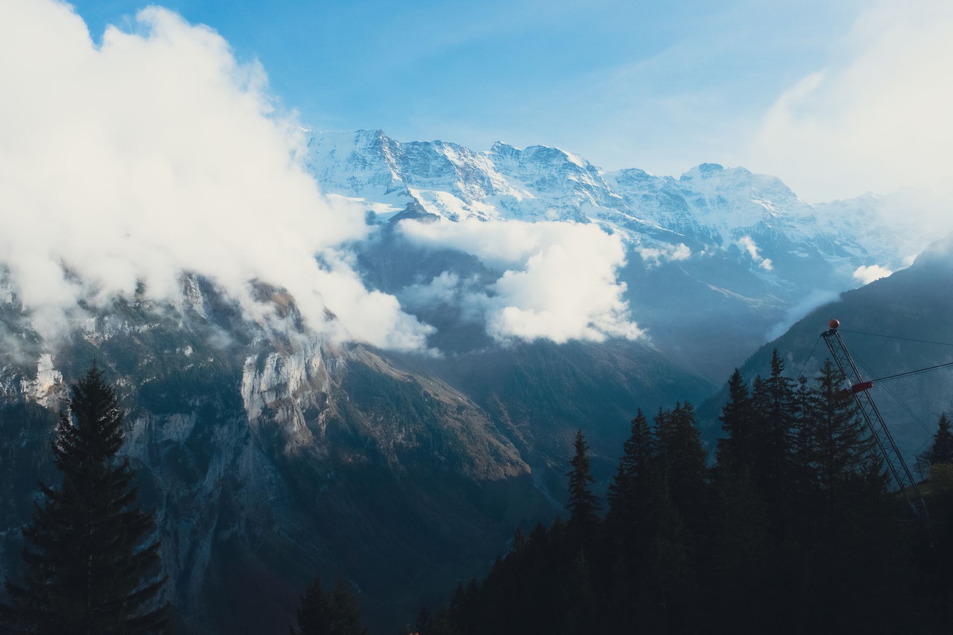 A breathtaking view of snowy mountain peaks partially shrouded in clouds with pine trees in the fore