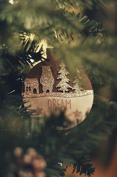 Glittering Christmas ornament with trees and house on a decorated tree, capturing festive ambiance.
