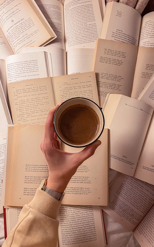 Person Holding a Cup of Coffee Near Books 