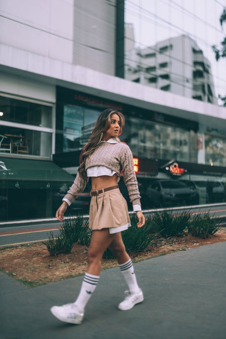 A Woman In Gray Sweater And Brown Skirt Walking On The Street