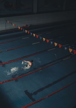Athlete swimming butterfly stroke in a dimly lit indoor pool, focused on training.