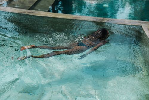 Free A woman swimming in a luxurious pool, creating ripples in the clear water under bright sunlight. Stock Photo