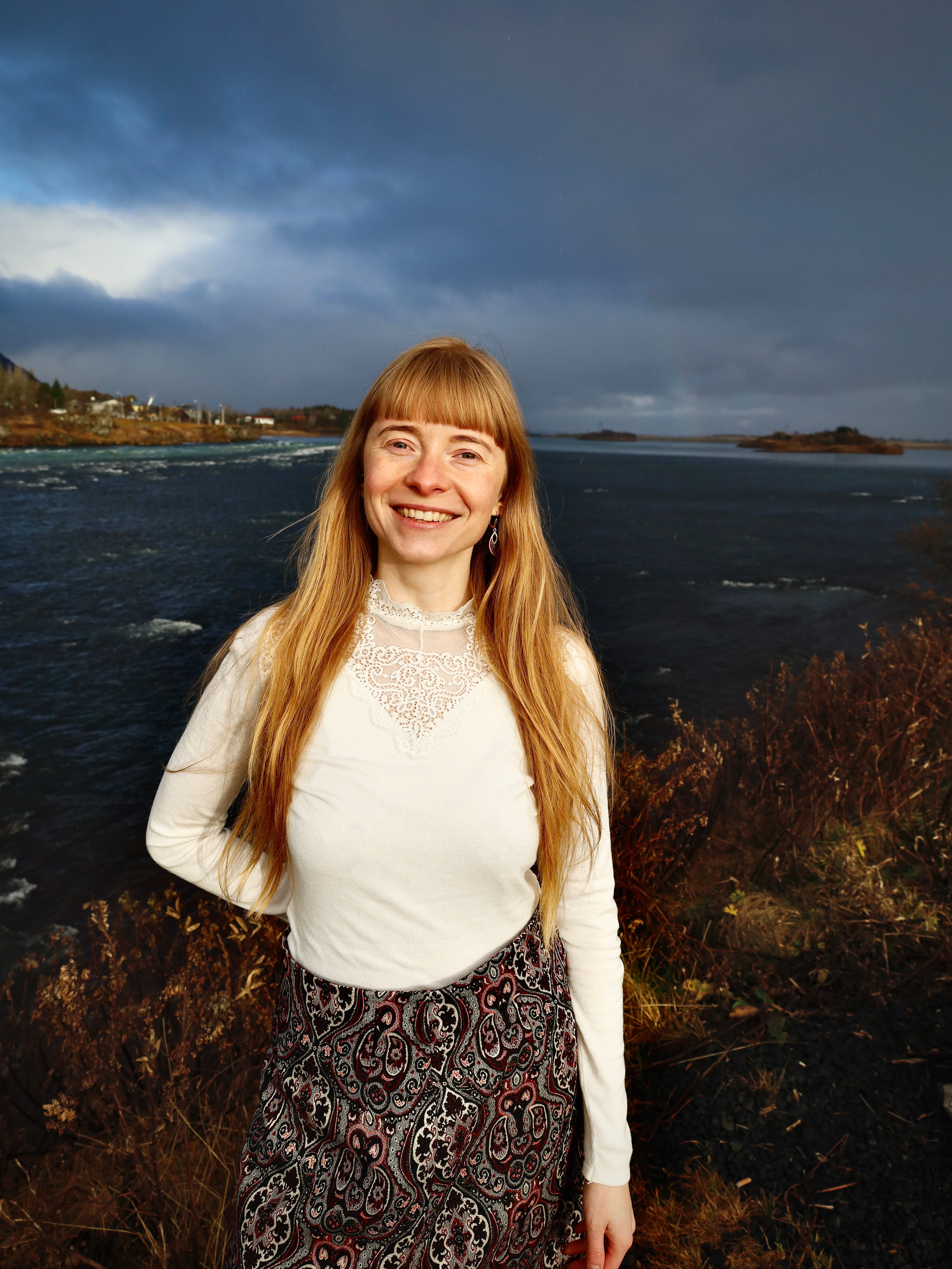 A happy woman in white blouse and skirt enjoys the scenic Icelandic lakeshore.