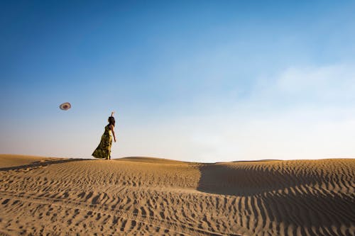 Free Woman Standing on Sand Dune Throwing Hat Stock Photo