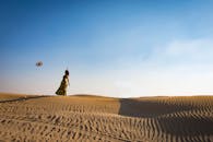 一名妇女独自站在迪拜的沙丘上，在晴朗的蓝天下将帽子抛向空中