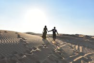 一对夫妇手牵着手，在迪拜沙漠的沙丘上奔跑，展现浪漫与冒险