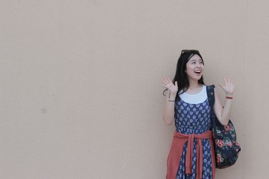 Young woman with a floral bag posing joyfully against a wall outdoors.