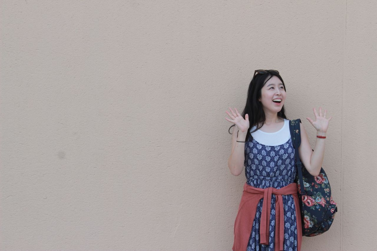 young woman with a floral bag posing joyfully against a wall outdoors