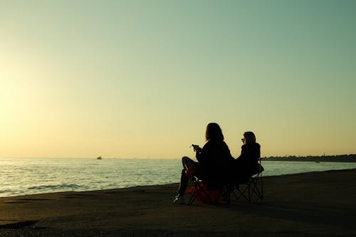 Silhouette of Two People Sitting on the Beach during Sunset