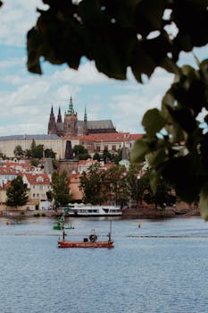 View of Prague Castle and Vltava River, framed by foliage. Perfect for travel and scenic photography.