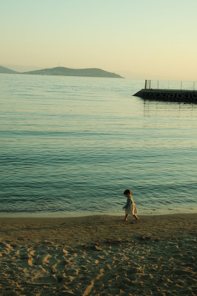 A Child Walking On A Beach At Sunset