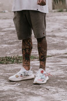 Close-up shot of tattooed legs in stylish white sneakers standing on a pavement in Brazil.