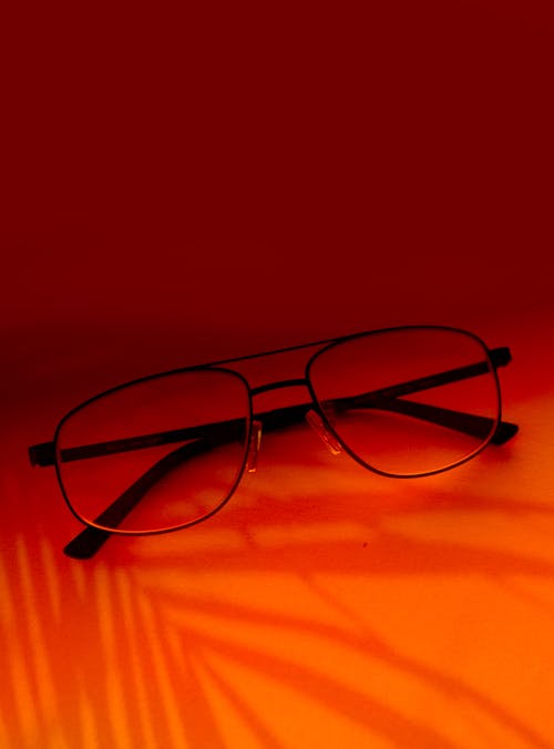 Free Eyeglasses with Black Frames Lying on Orange Surface Stock Photo