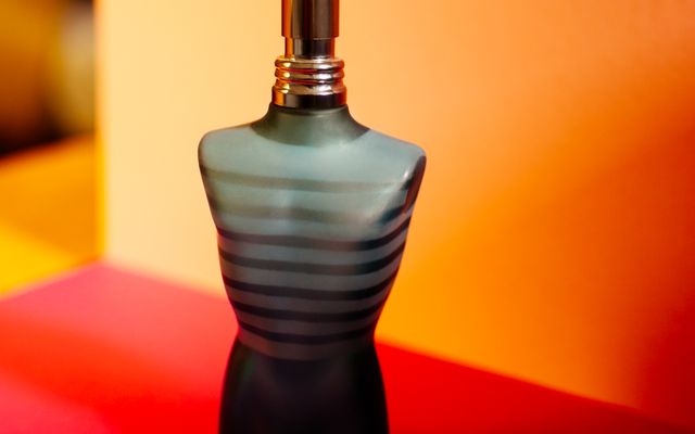 Striped torso-shaped cologne bottle standing on a bright red and orange background
