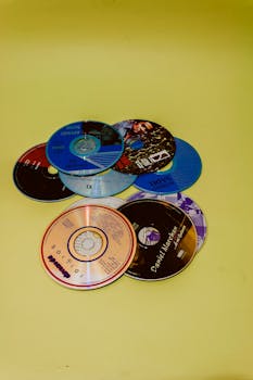 Flat lay of various CDs on a vibrant yellow surface, showcasing music diversity.