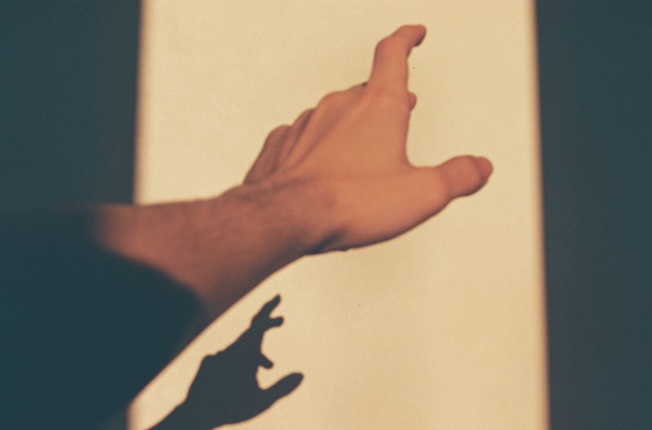 A close-up of a hand reaching towards a light source, casting a shadow.