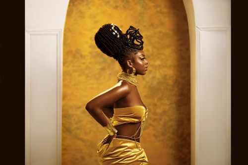 Free Profile of woman in elegant gold attire posing indoors against a golden backdrop. Stock Photo