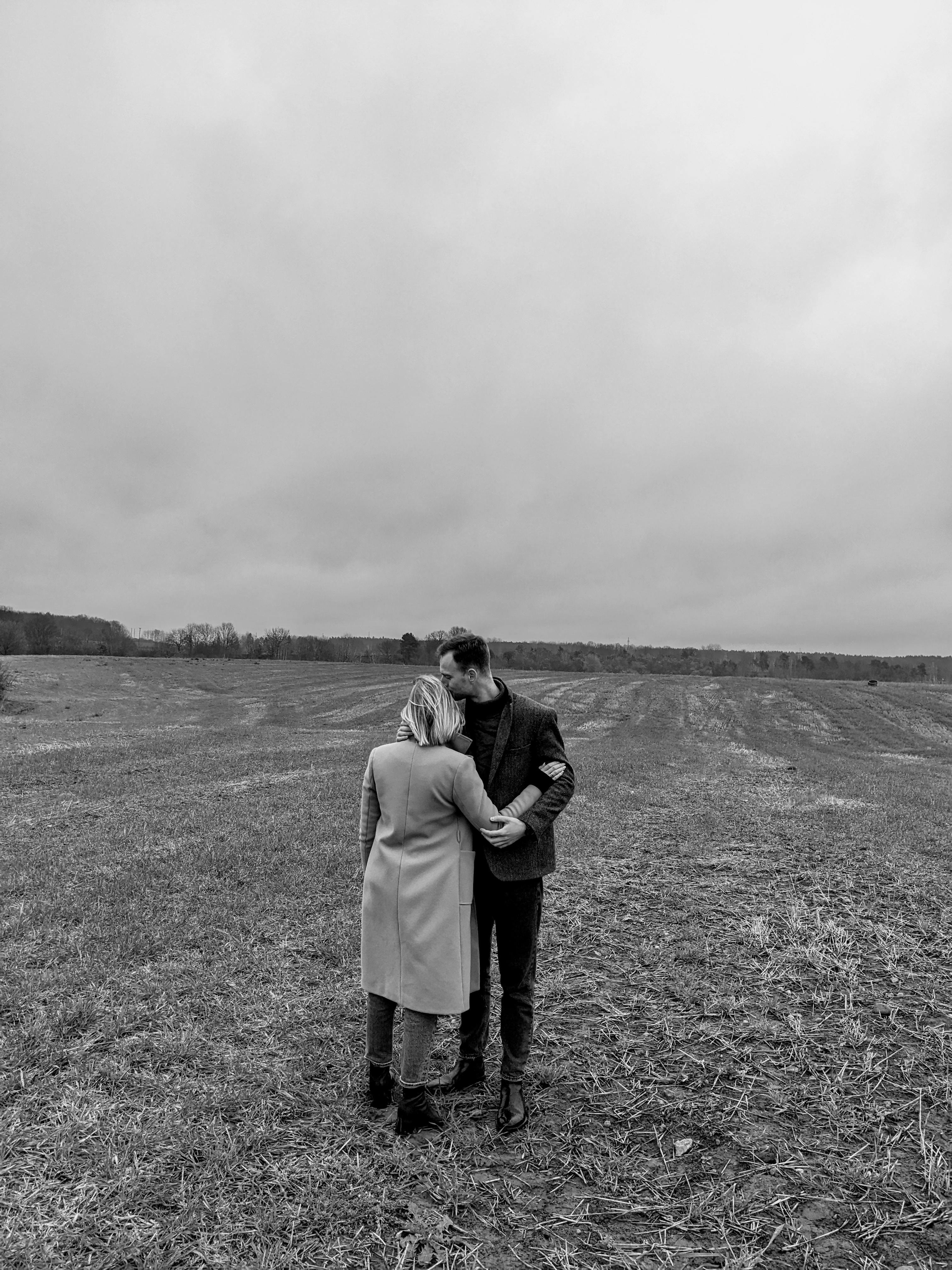 A couple embraces in a wide open rural field under a cloudy sky in Grodno, Belarus.
