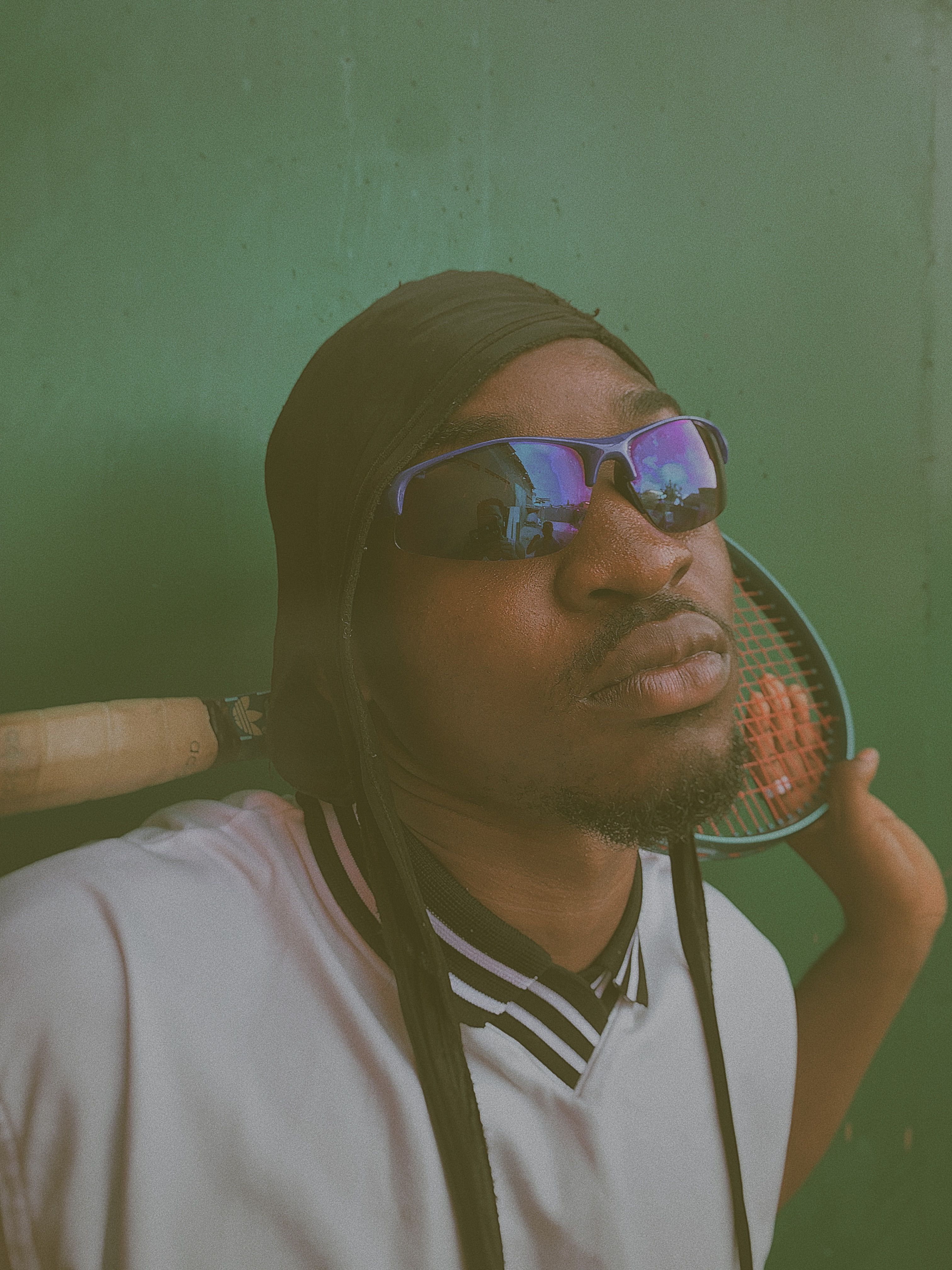 A stylish man with sunglasses holding a tennis racket outdoors.