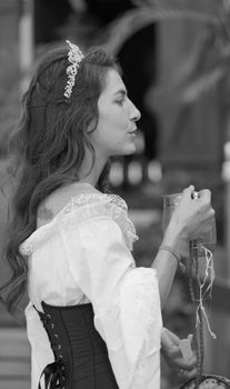 Black and white profile portrait of a woman in a vintage costume holding a drink at an outdoor event.